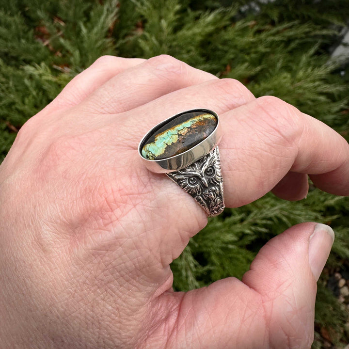 Handcrafted sterling silver owl ring with blackjack turquoise cabochon shown on hand. Made in Fort Collins, Colorado.