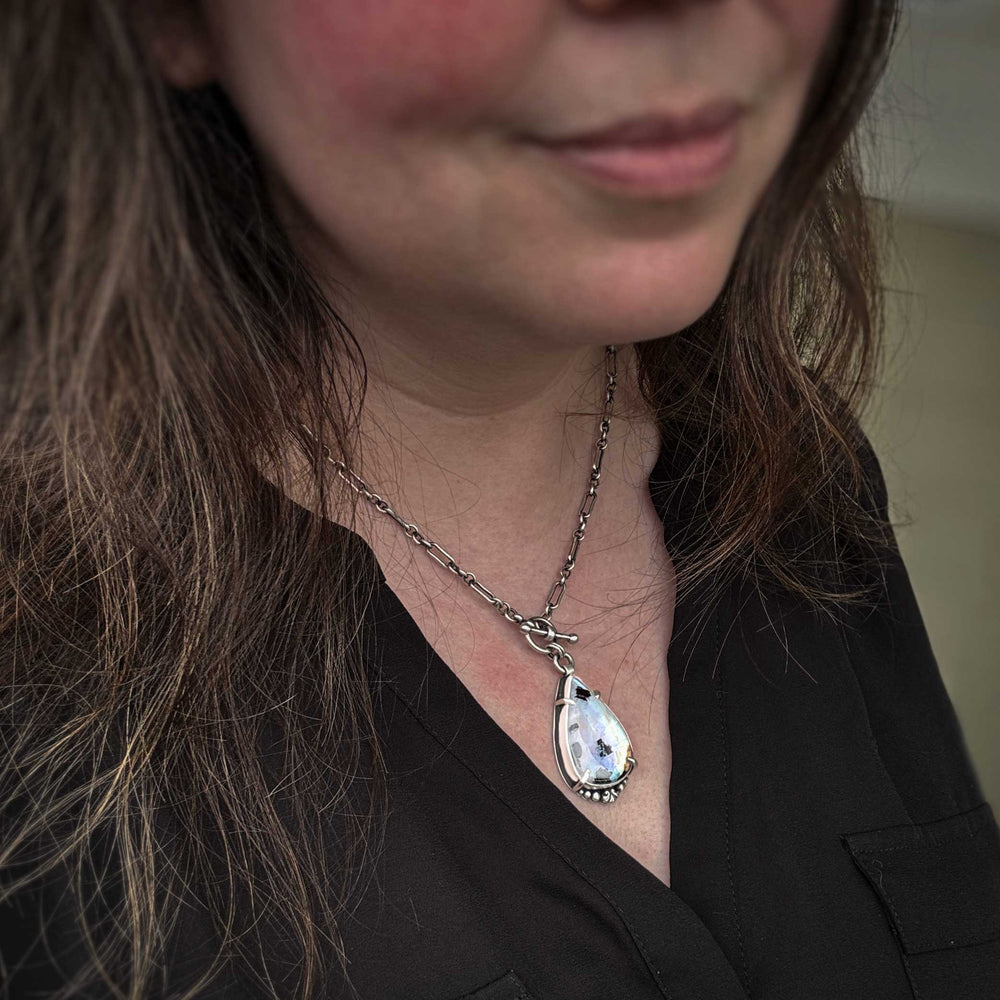 Rainbow moonstone statement necklace worn on model showing sterling silver chain and pendant scale. Close-up of a person wearing a necklace with a teardrop-shaped pendant.