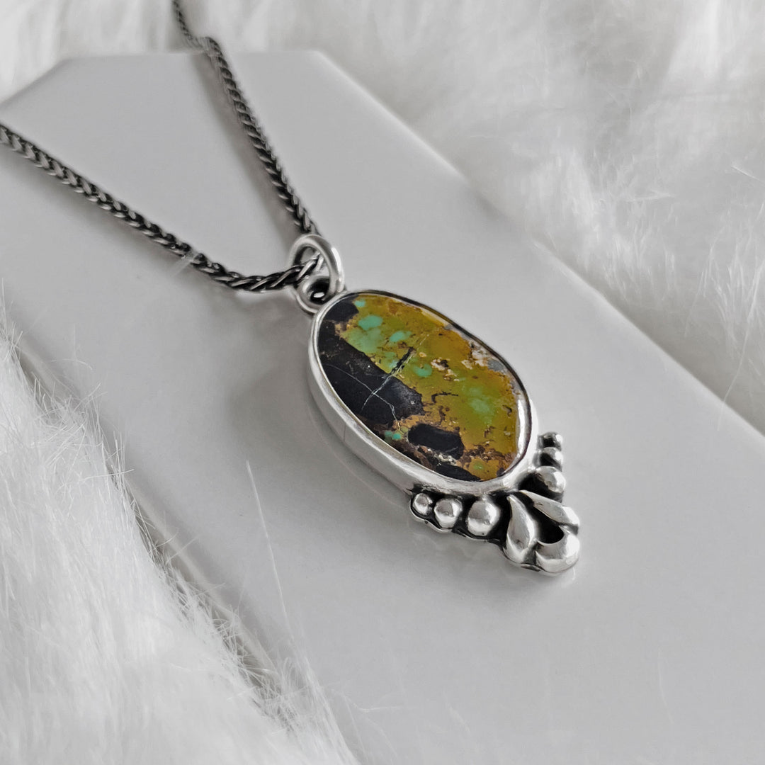 Side view of handmade turquoise pendant in sterling silver with detailed bezel and decorative elements.