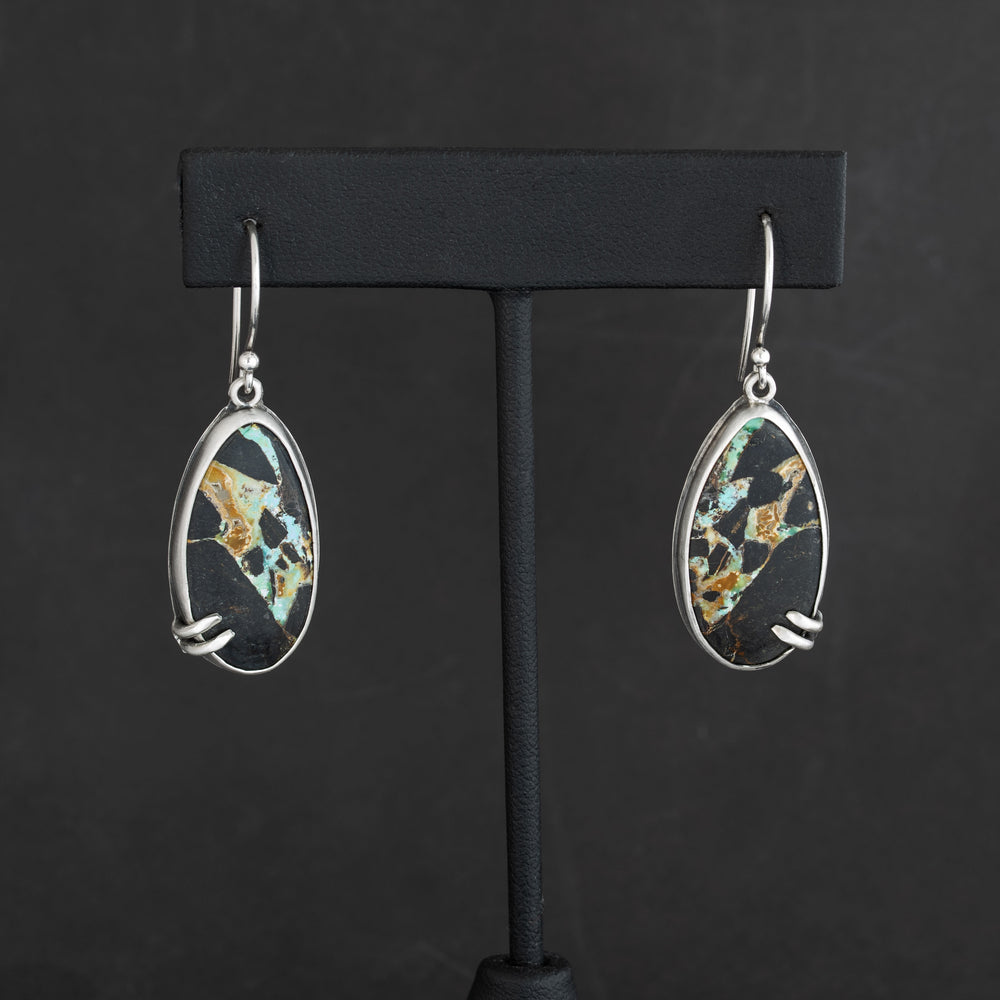 Blackjack turquoise dangle earrings set in handcrafted sterling silver, displayed on a matte black jewelry stand.