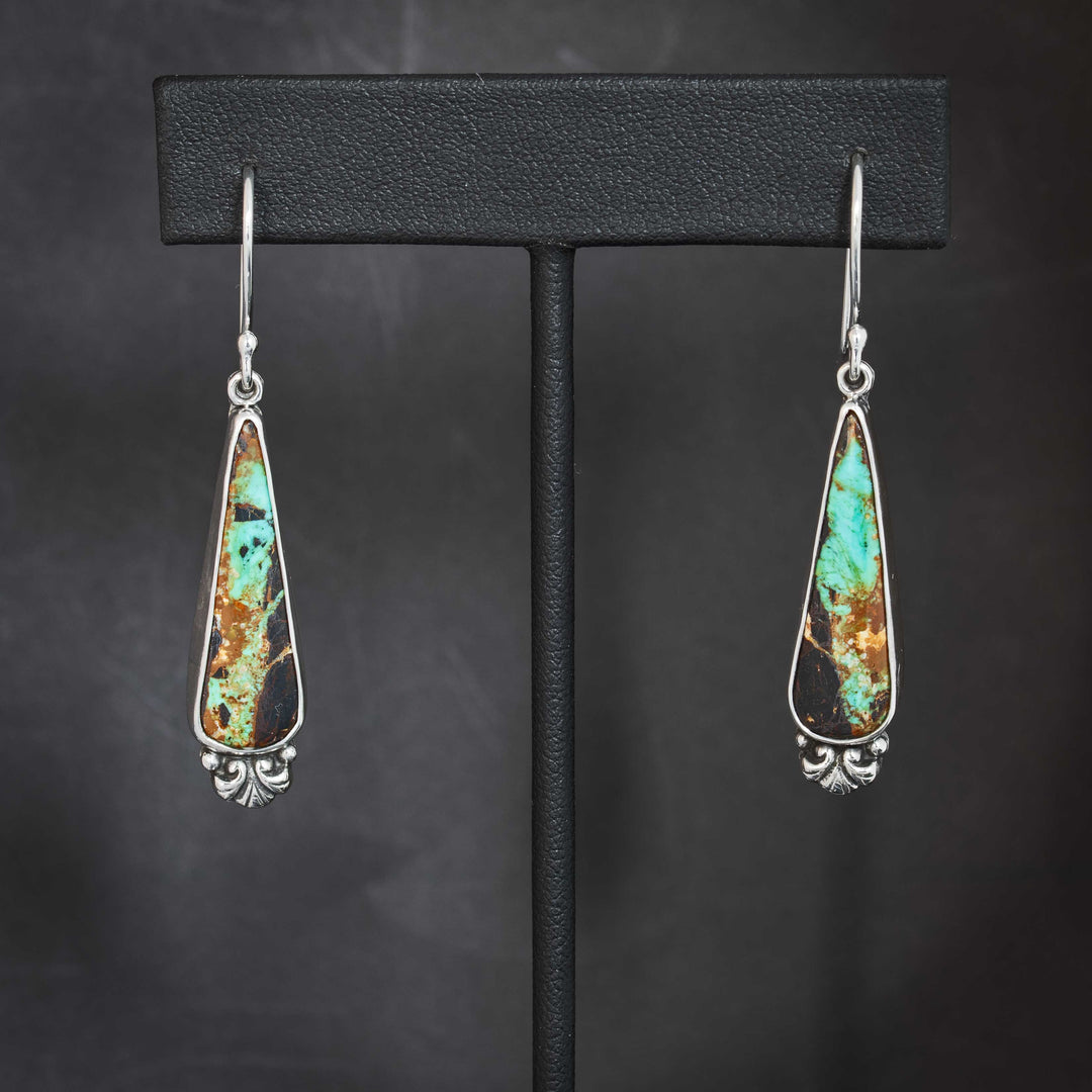 Handmade sterling silver drop earrings with Black Jack turquoise teardrop stones, showcasing bright turquoise veining and dark matrix with Art Nouveau scroll detail.