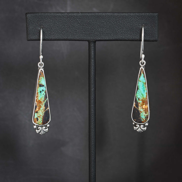 Handmade sterling silver drop earrings with Black Jack turquoise teardrop stones, showcasing bright turquoise veining and dark matrix with Art Nouveau scroll detail.