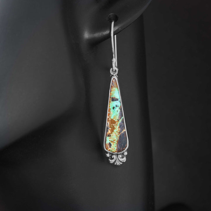 Close-up of Black Jack turquoise earrings worn, handmade sterling silver teardrops featuring vivid turquoise veining and organic brown matrix.