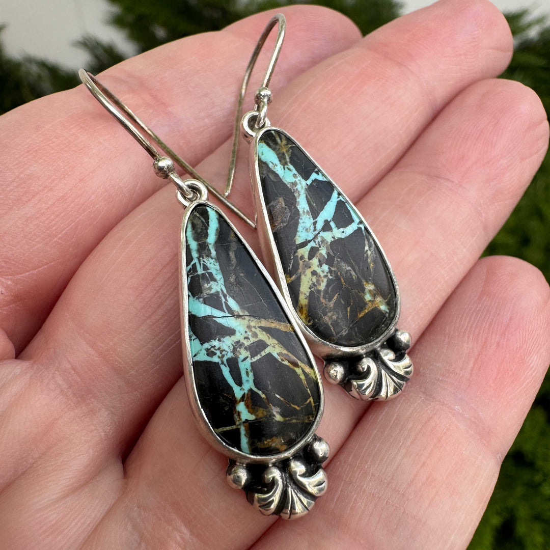 Fanned view of Blackjack turquoise teardrop earrings in hand showing scroll base detail and fine silver granules, artisan sterling silver earrings