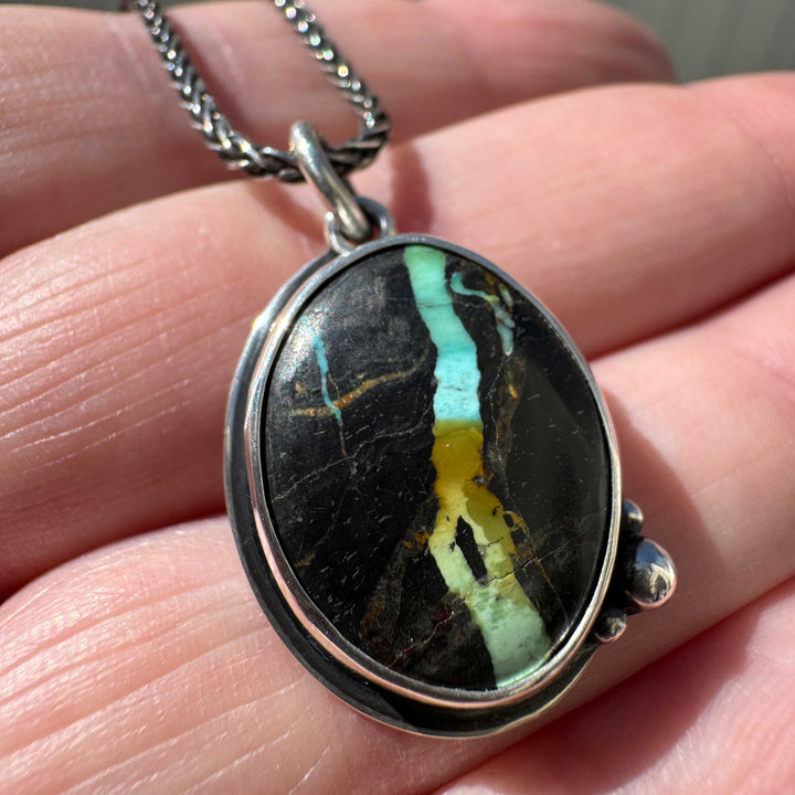 Detail view of rare Blackjack turquoise pendant showing teal, cyan, gold and green ribbon veining through near-black chert matrix, handcrafted sterling silver
