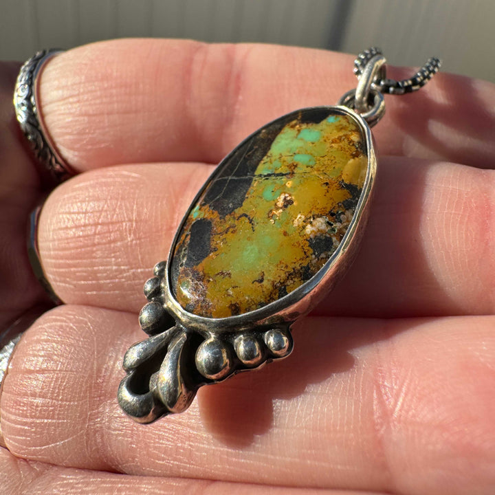 Blackjack Turquoise stone pendant on silver chain held between fingers