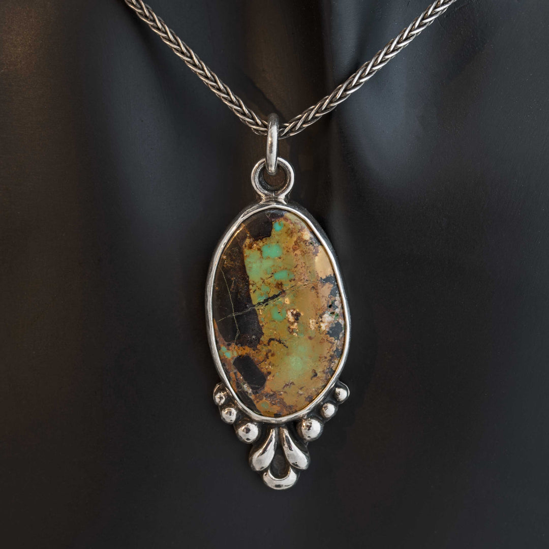 Handcrafted Blackjack turquoise pendant in sterling silver with botanical motif, shown on a woven chain.