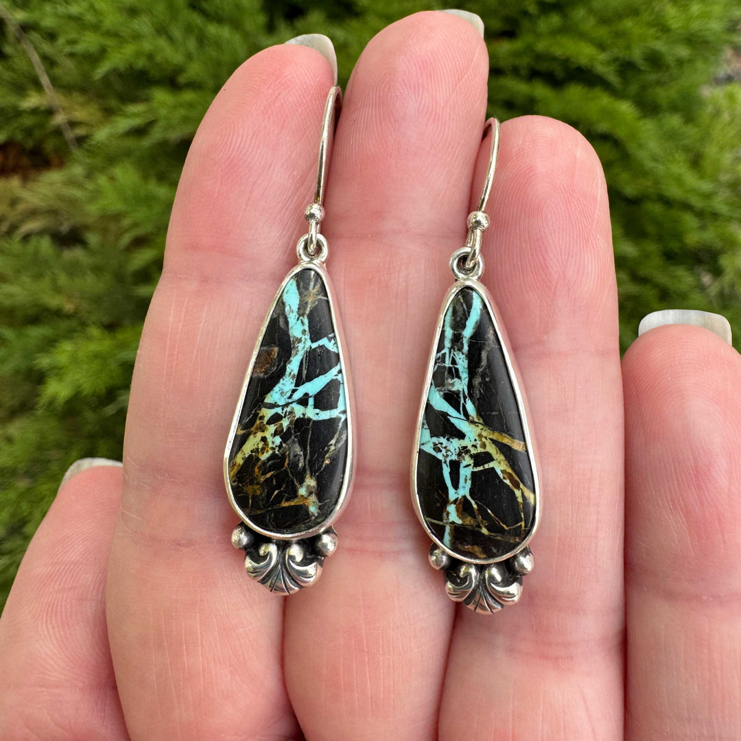 Close-up of Blackjack turquoise teardrop earrings showing teal lightning bolt matrix, sterling silver scroll and granule detail at base, artisan silversmith Colorado