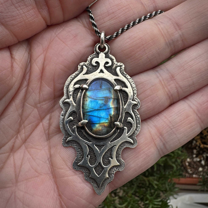Handcrafted silver labradorite pendant in hand showing scale and ornate metalwork details
