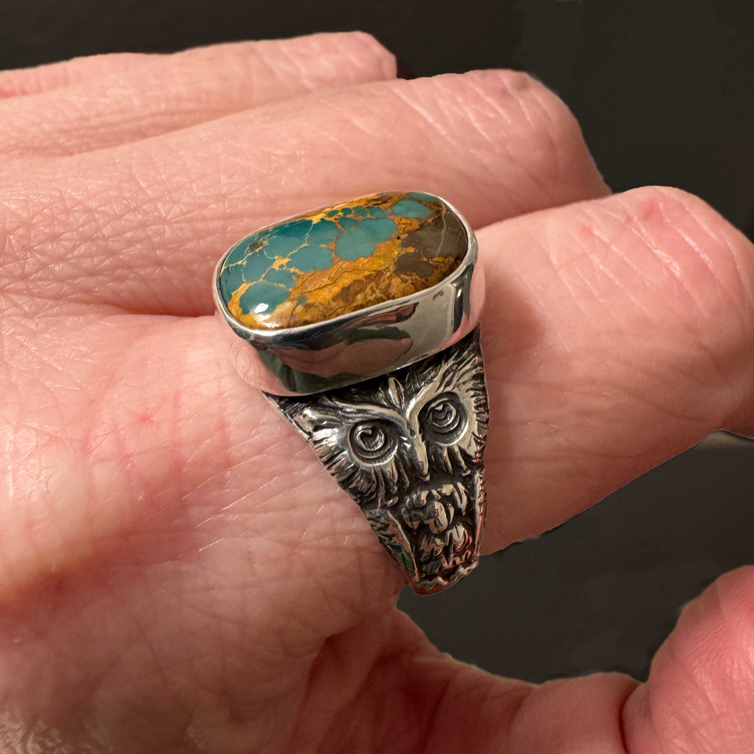 Royston Ribbon turquoise silver owl ring with a turquoise stone on a person's finger against a dark background