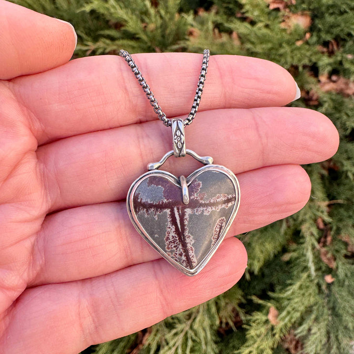 Handmade sterling silver heart necklace with dendritic rhyolite stone held in hand