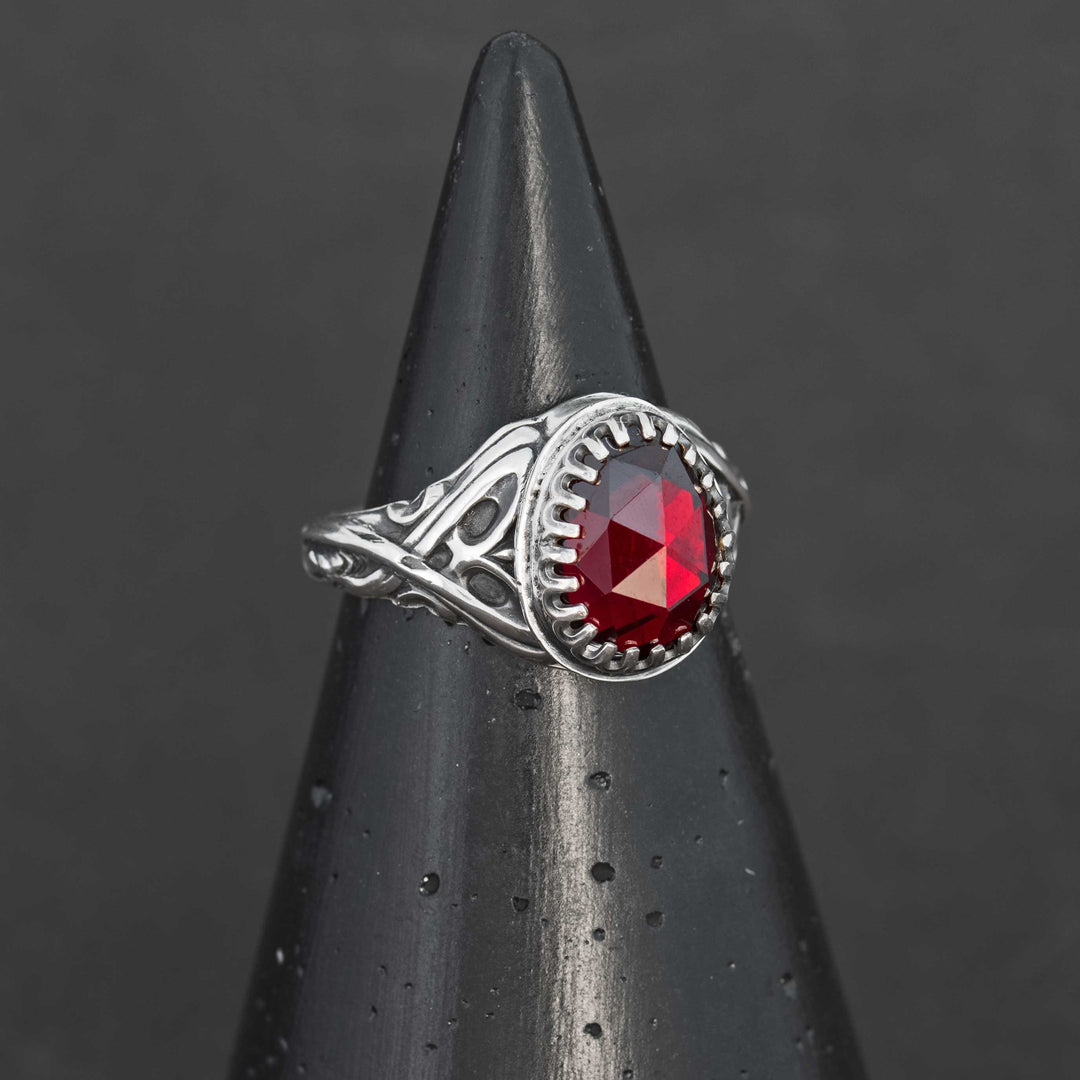 Side-angle view of a sterling silver garnet ring with ornate elven-style scrollwork and a rosecut Mozambique garnet.