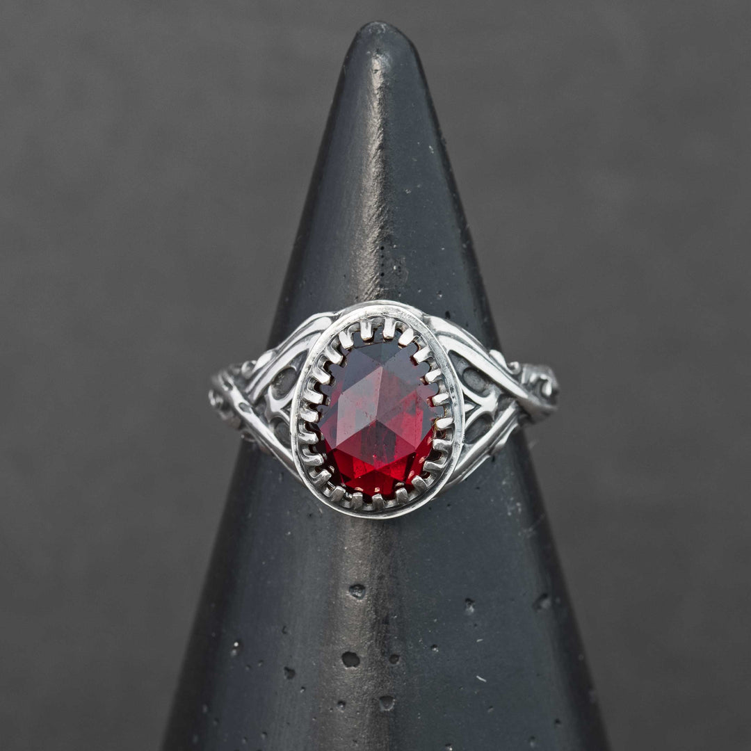 Handcrafted sterling silver fantasy scrollwork ring featuring a deep red Mozambique garnet, shown on a ring cone.