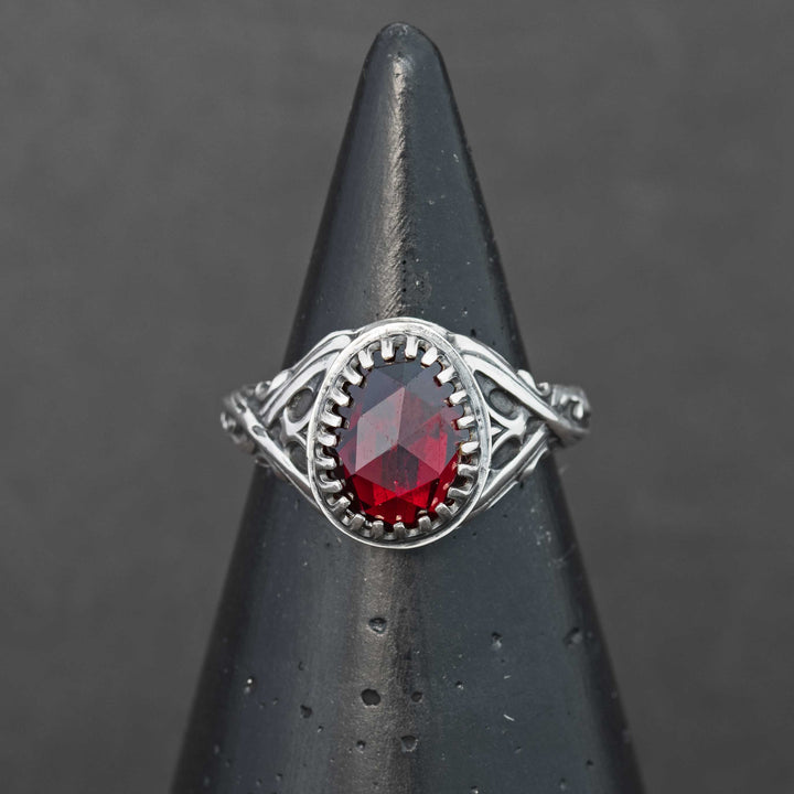 Handcrafted sterling silver fantasy scrollwork ring featuring a deep red Mozambique garnet, shown on a ring cone.