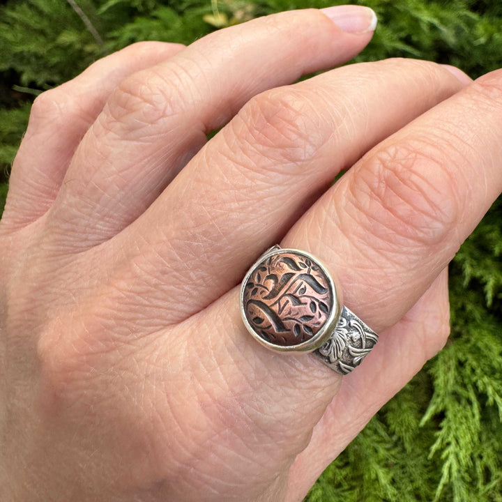 Close-up of a copper Gothic letter E impression framed in a sterling silver bezel on a handmade initial ring.
