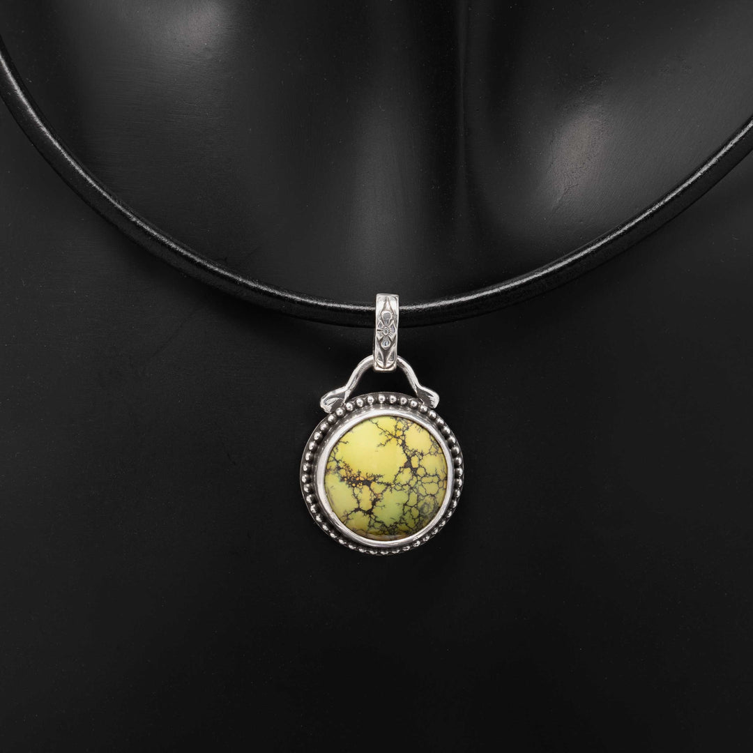 Round green turquoise pendant in a sterling silver beaded setting on a black leather cord.