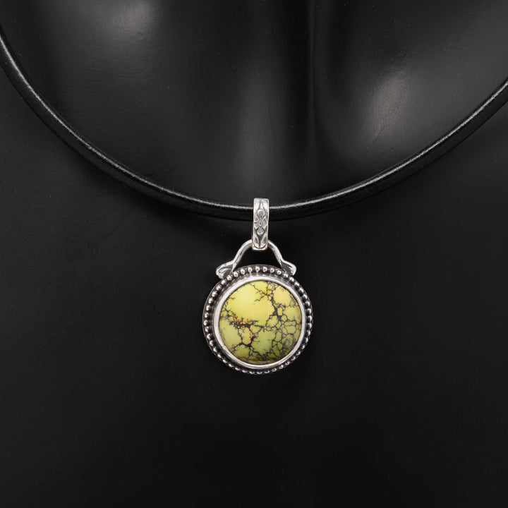 Round green turquoise pendant in a sterling silver beaded setting on a black leather cord.