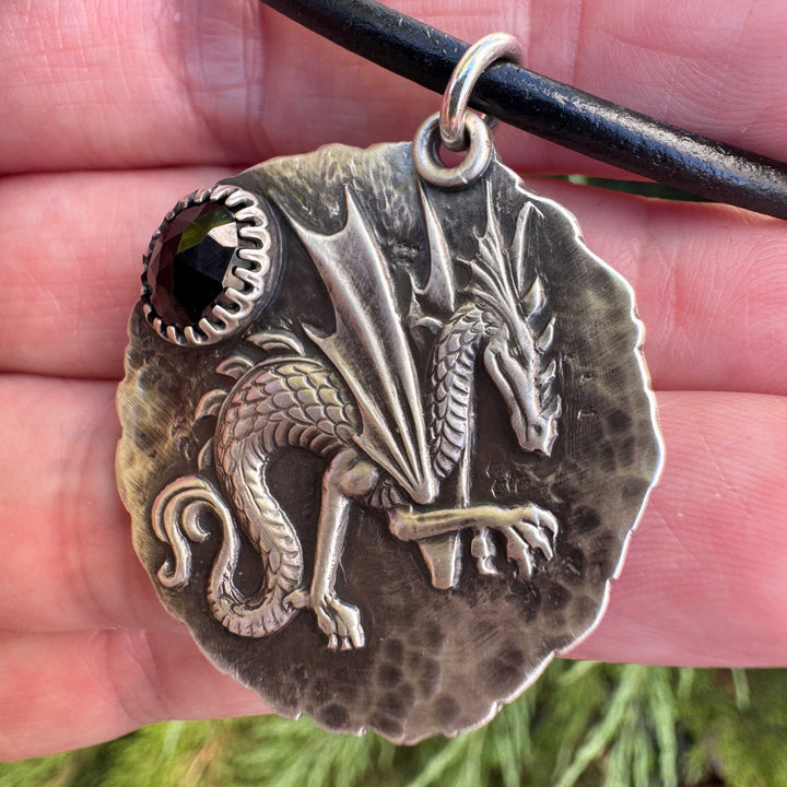 Closeup of a handmade sterling silver dragon talisman with black spinel worn on a black leather cord