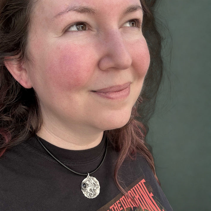 Handmade sterling silver dragon talisman with black spinel worn on a black leather cord shown on model