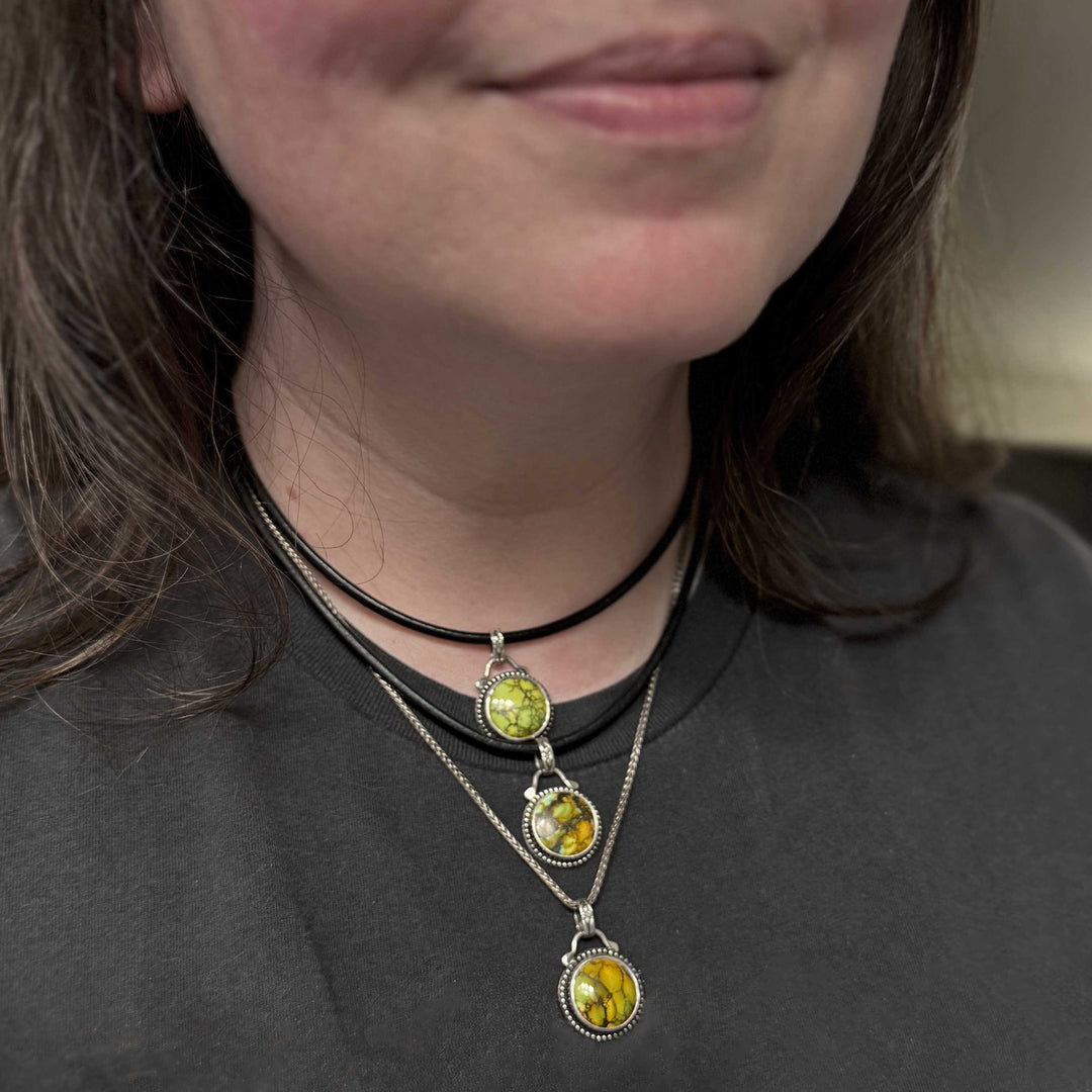 Layered green turquoise pendants worn on black and silver chains.