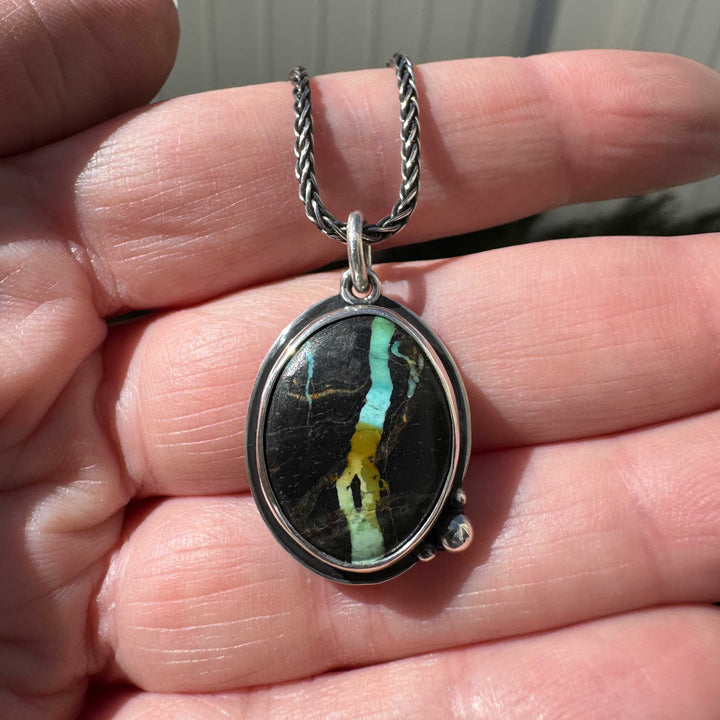Close-up of Blackjack turquoise oval pendant in sterling silver bezel with granule detail, multicolor ribbon stone on oxidized wheat chain