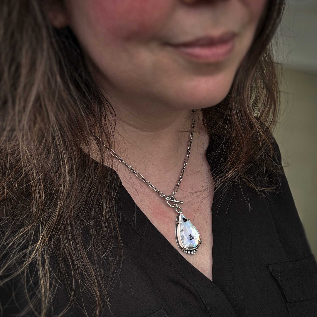 Rainbow moonstone statement necklace worn on model showing sterling silver chain and pendant scale. Close-up of a person wearing a necklace with a teardrop-shaped pendant.