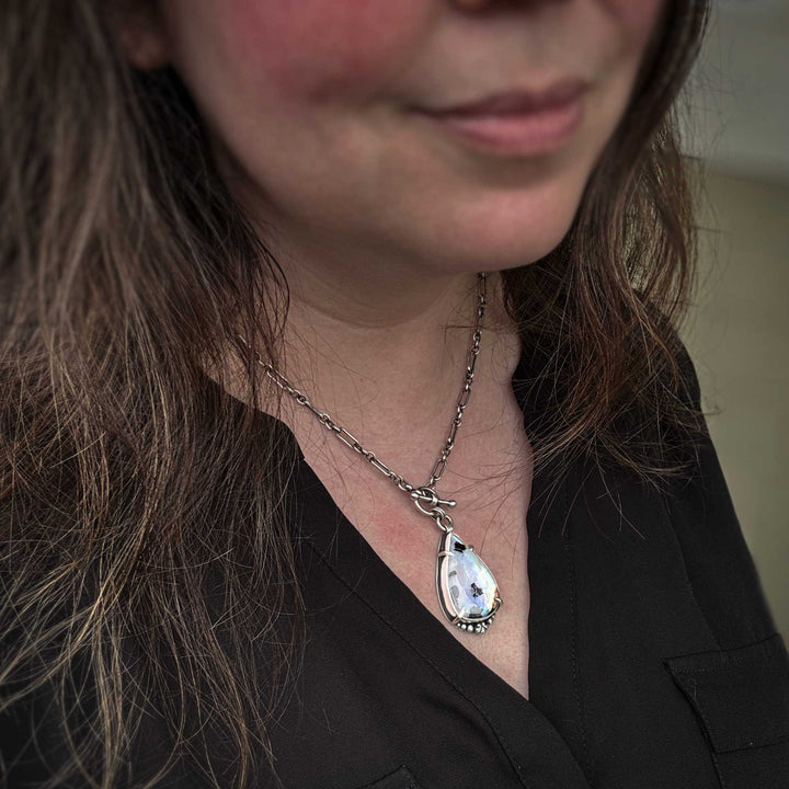 Rainbow moonstone statement necklace worn on model showing sterling silver chain and pendant scale. Close-up of a person wearing a necklace with a teardrop-shaped pendant.