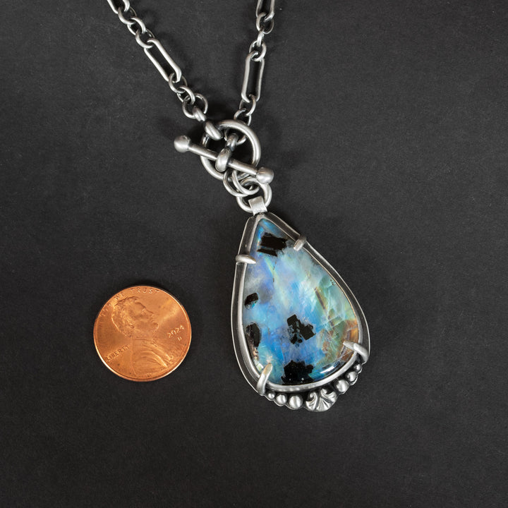 Rainbow moonstone and black tourmaline pendant on black background with penny for size reference.