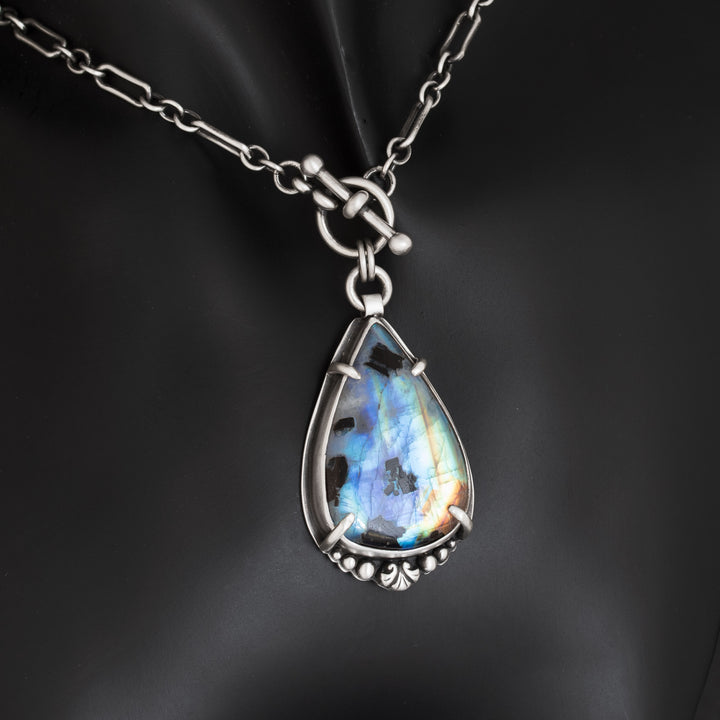 Rainbow moonstone pendant with dramatic blue flash on black background highlighting gemstone fire