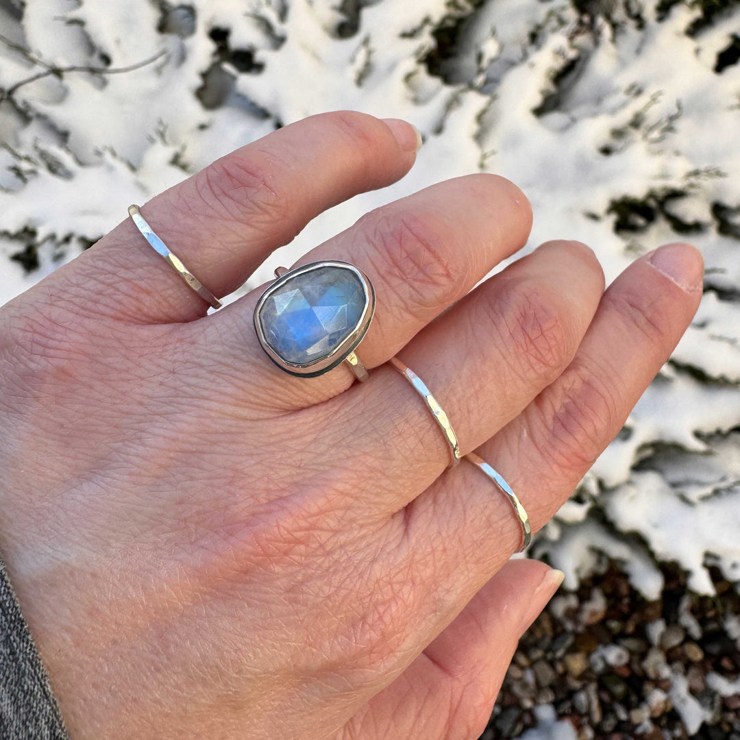 Rose cut rainbow moonstone ring size 6.5 egg shape worn on hand with hammered stacker bands, snowy background