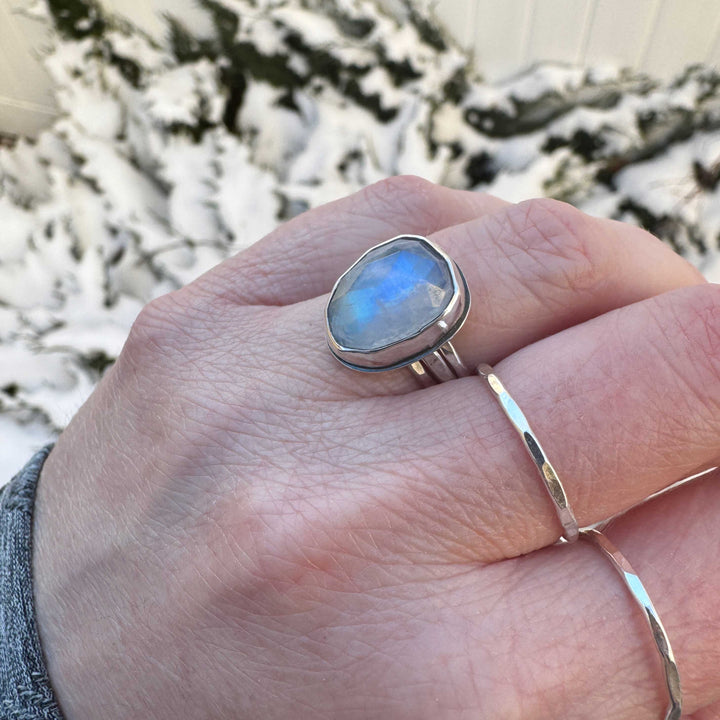 Close up of rose cut rainbow moonstone ring size 6.5 stacked with hammered sterling silver bands, strong blue flash
