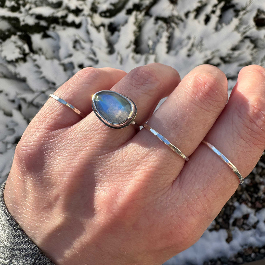 Rose cut rainbow moonstone ring size 6 worn on hand with hammered stacker bands, snowy background