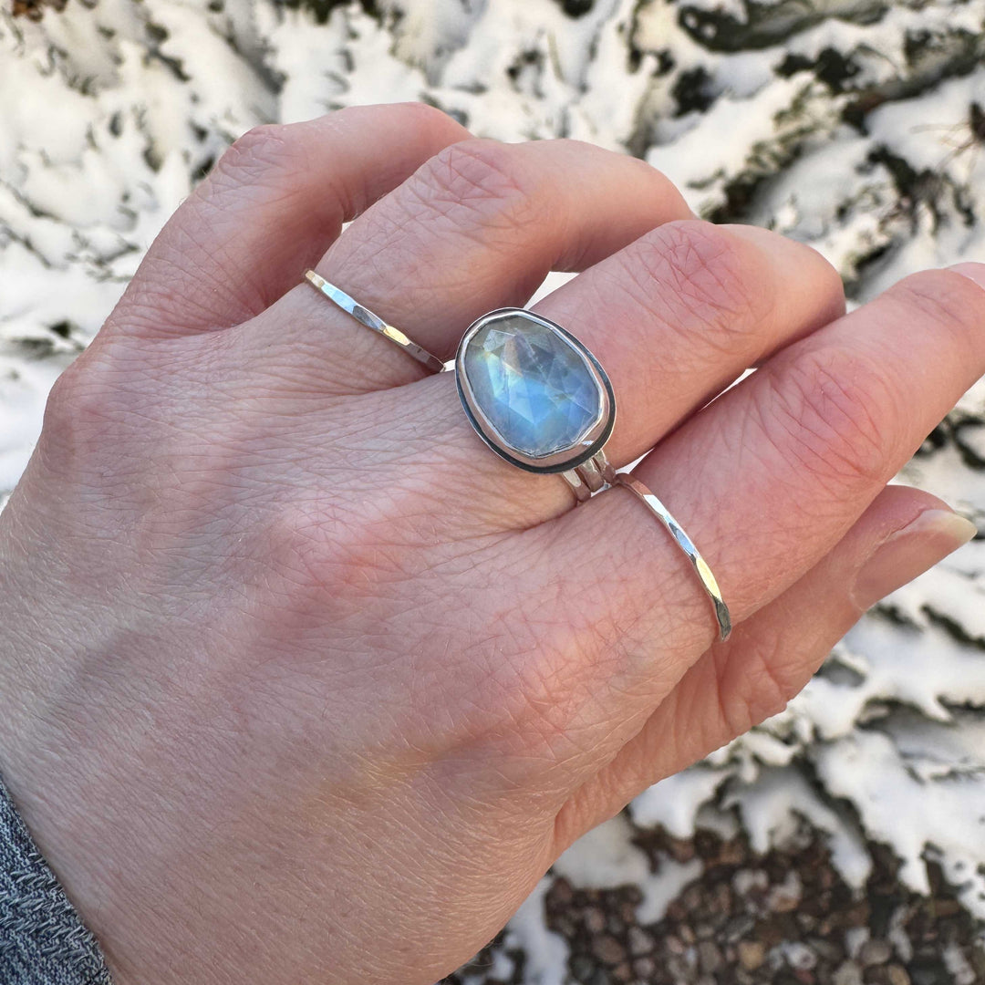 Handmade rose cut rainbow moonstone ring size 7.5 worn on hand outdoors with hammered stacker rings, winter background