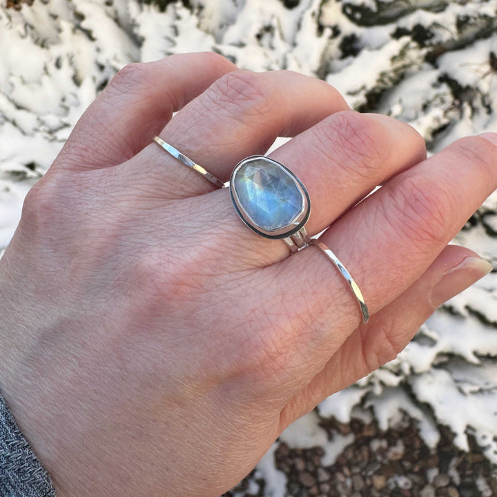 Handmade rose cut rainbow moonstone ring size 7.5 worn on hand outdoors with hammered stacker rings, winter background