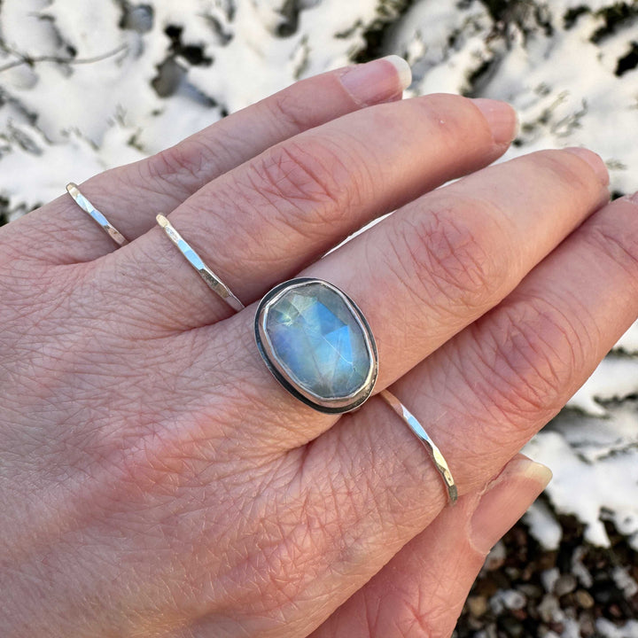 Rose cut rainbow moonstone ring size 7.5 horizontal egg shape worn on hand with hammered stacker bands, snowy background