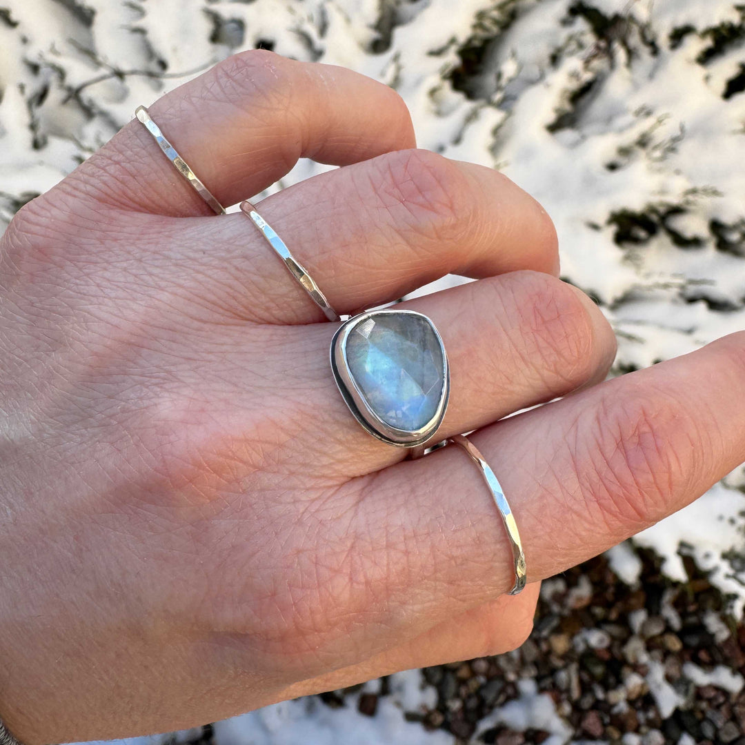 Rose cut rainbow moonstone ring on hand with stacker bands, blue flash visible, winter outdoor setting
