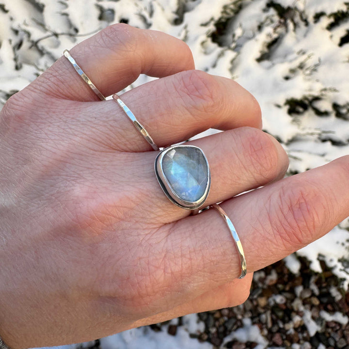 Rose cut rainbow moonstone ring on hand with stacker bands, blue flash visible, winter outdoor setting