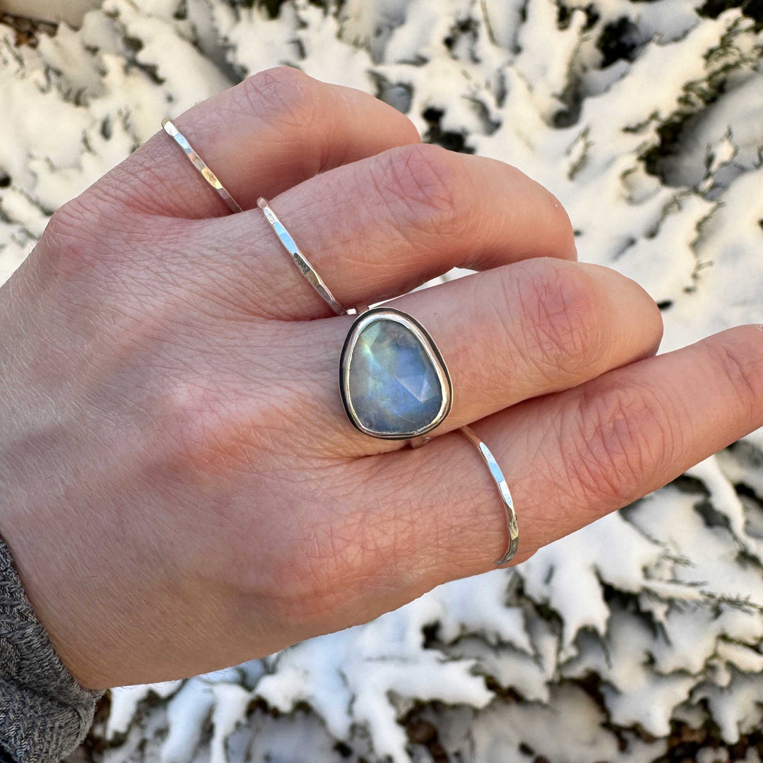 Rose cut rainbow moonstone sterling silver ring worn on hand with hammered stacker bands, snowy background