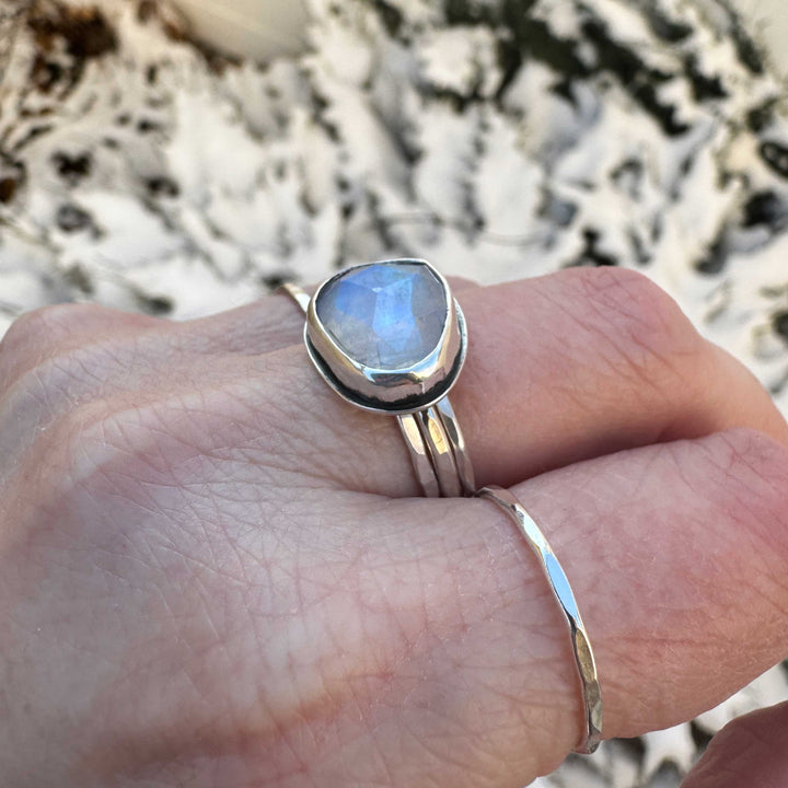 Close up of rose cut rainbow moonstone ring stacked with hammered sterling silver bands