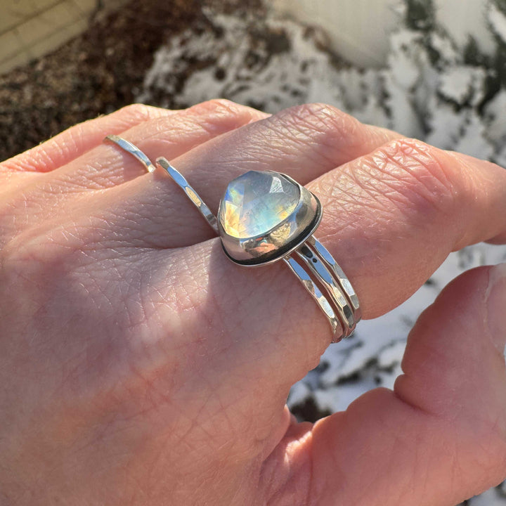 Close up of rose cut rainbow moonstone ring size 9.5 stacked with hammered sterling silver bands, deep blue-purple and orange flash
