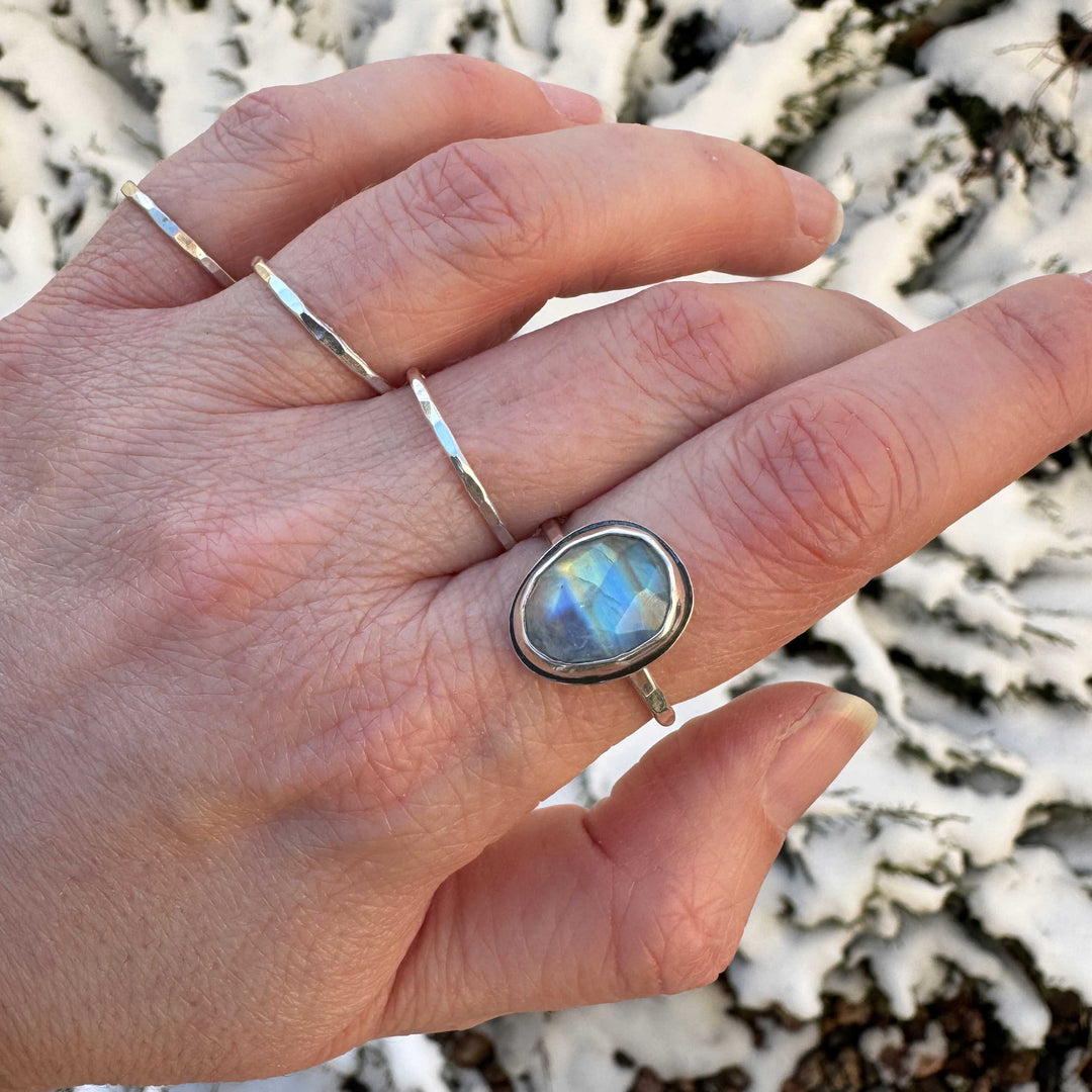 Rose cut rainbow moonstone ring size 9 worn on hand with hammered stacker bands, multiple blue flash hues visible, snowy background