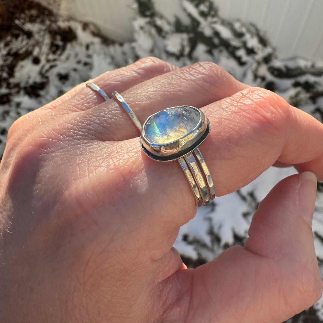 Close up of rose cut rainbow moonstone ring size 9 stacked with hammered sterling silver bands, vivid blue and gold flash