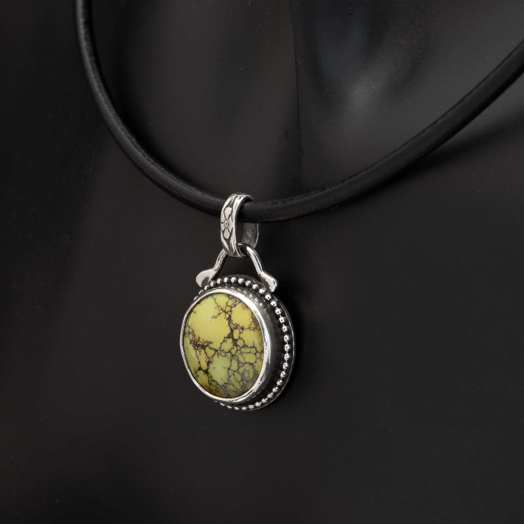 Side view of a handmade round turquoise necklace with an oxidized sterling silver bezel.
