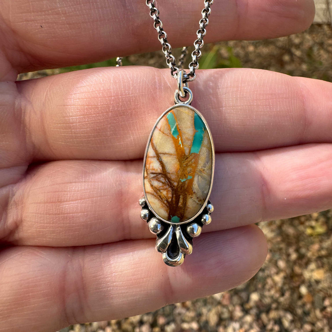 Custom Royston Ribbon pendant necklace in sterling silver, held in hand in natural light