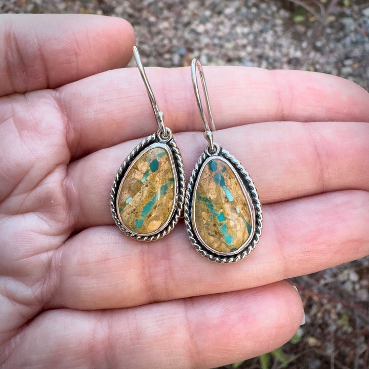 Handmade Royston Ribbon turquoise earrings held in hand, showing unique turquoise veining across golden-brown matrix.