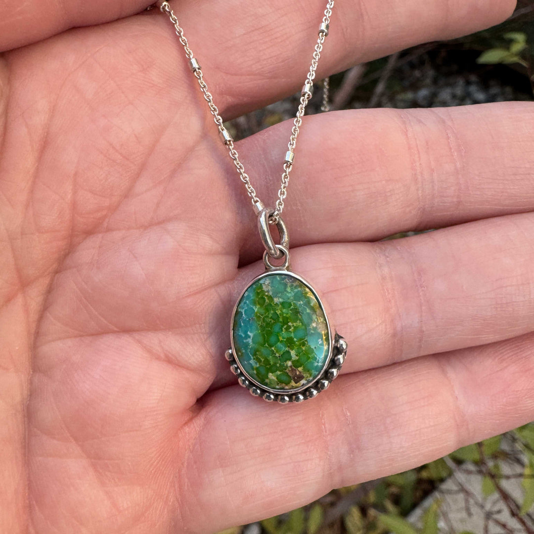 Small Sonoran Gold turquoise pendant with green and blue gemstone held in hand, sterling silver necklace.