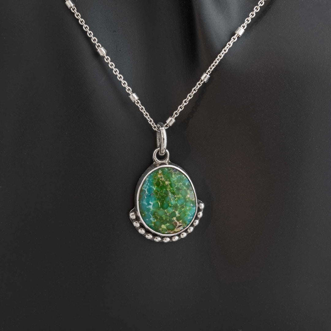 Handmade Sonoran Gold turquoise pendant necklace in sterling silver with pebble border on display.