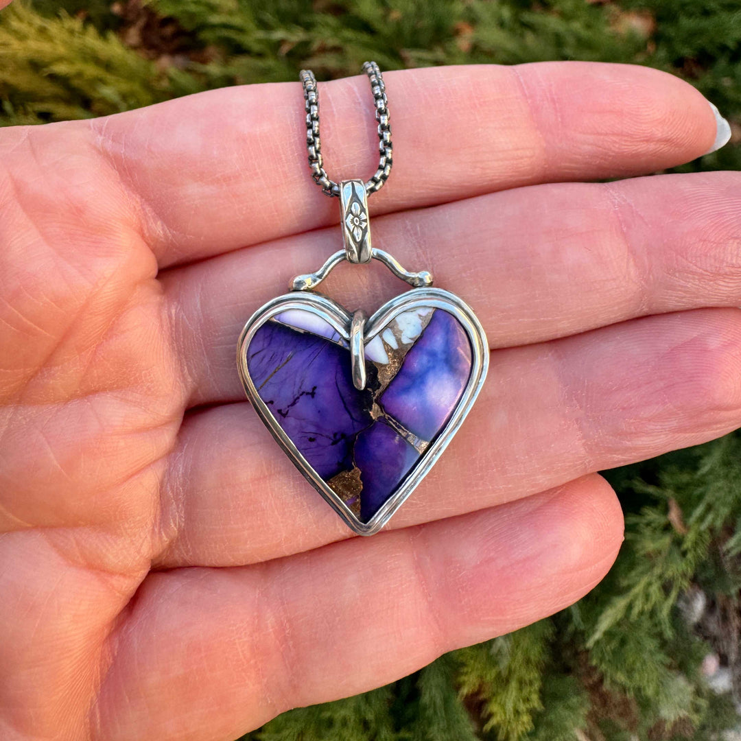 Heart-shaped purple pendant with silver frame held in a hand against a natural background