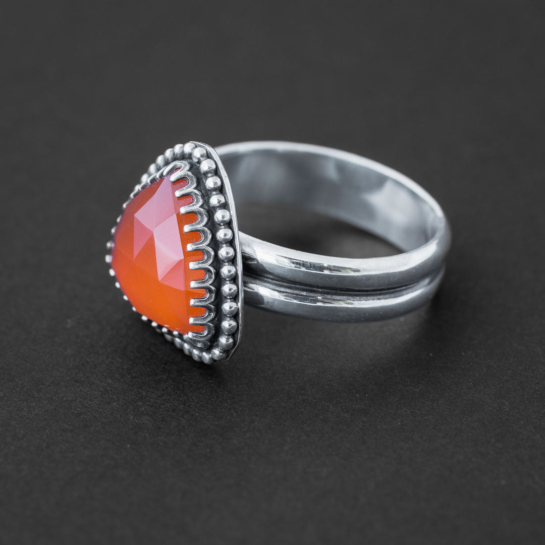 A carnelian crystal ring in sterling silver featuring a trillion cut bright orange gemstone.