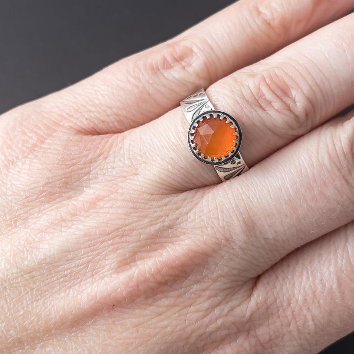 A hand modeling a sterling silver carnelian ring. The ring band is hand stamped with a flourish design. Made in Fort Collins, CO. 